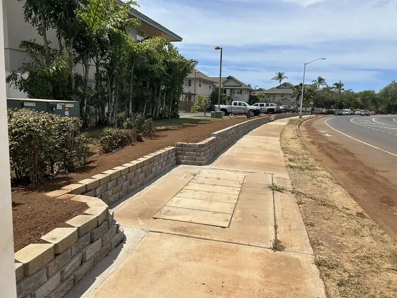 Finished dry-stack block retaining wall running alongside a concrete walkway and roadway