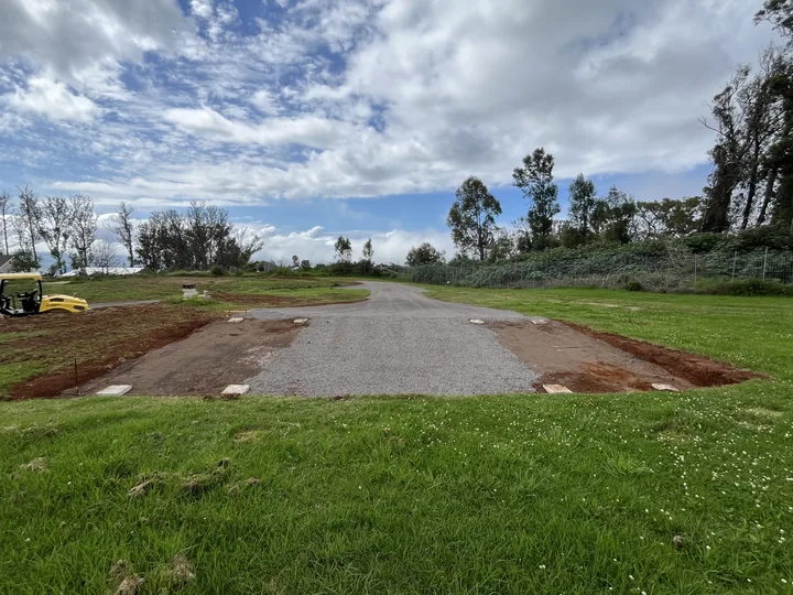Level gravel pad cut into a grassy Upcountry lot for a storage container, with a gravel driveway leading to it