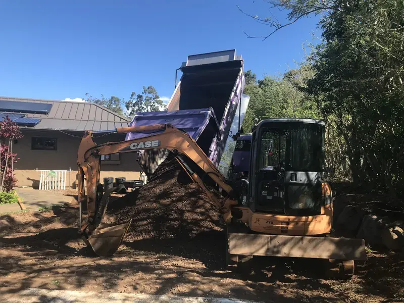 Dump truck tipping a load beside a CASE excavator on a Maui job site