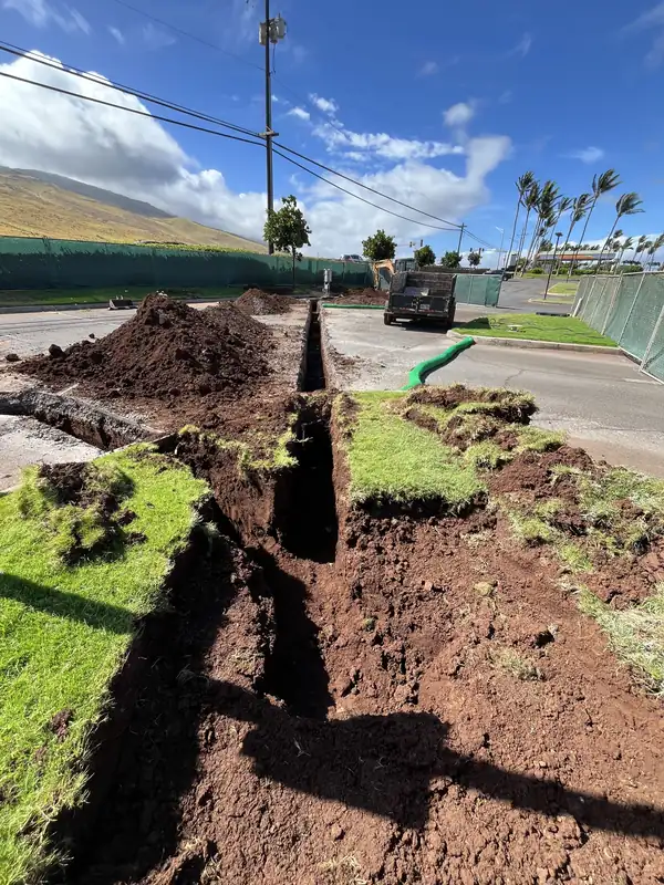Utility trench cut through a grass median beside a road, with conduit visible at the far end