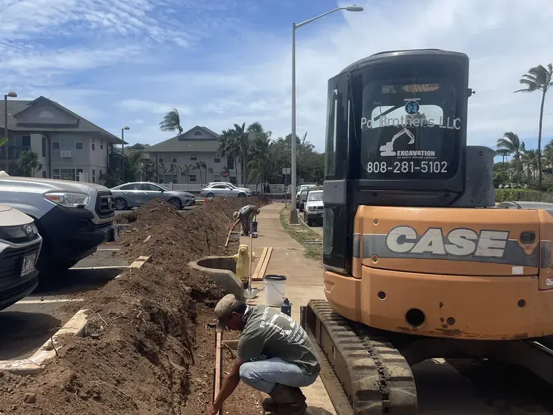 Po Brothers excavator digging the foundation for a block retaining wall beside a residential walkway