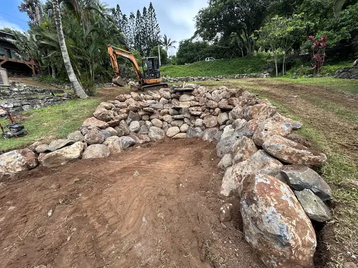 Large boulders set in a curved wall around a waterfall excavation on a sloped lawn